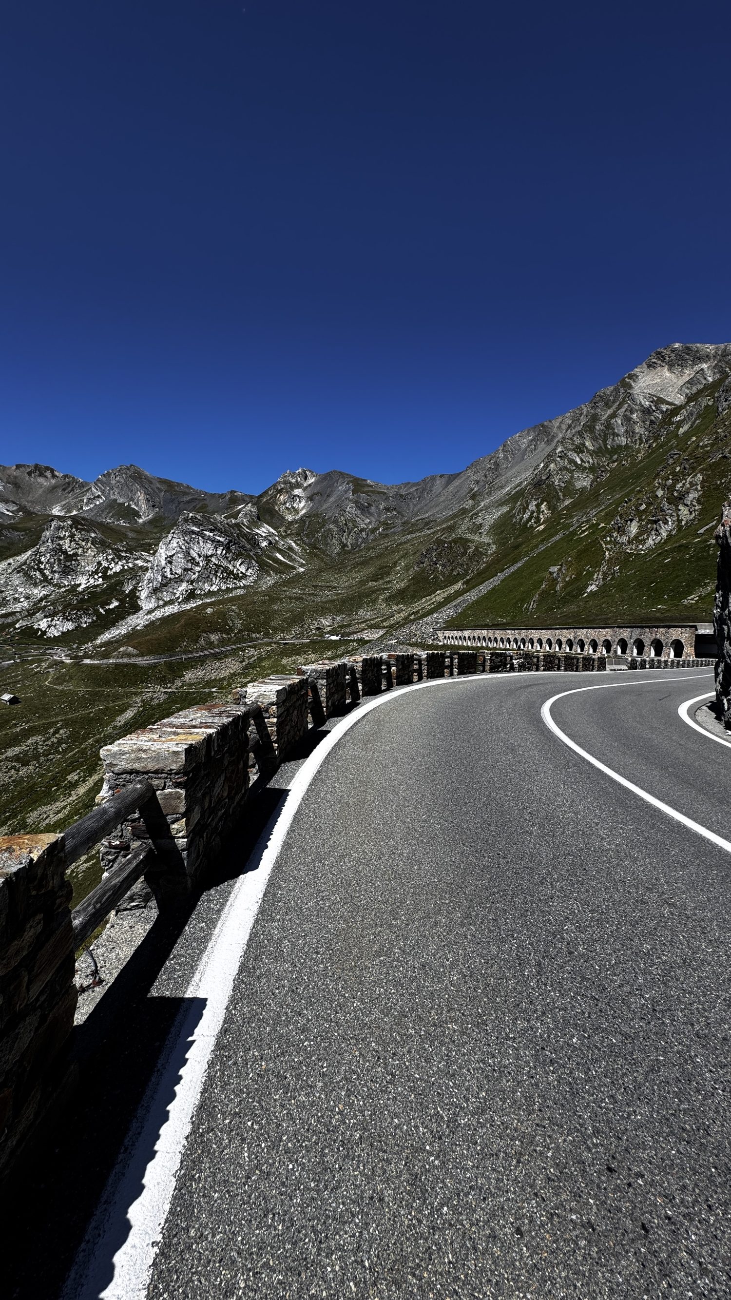 Route de col en lacets bordée d'un mur de pierres sèches, dans les Alpes